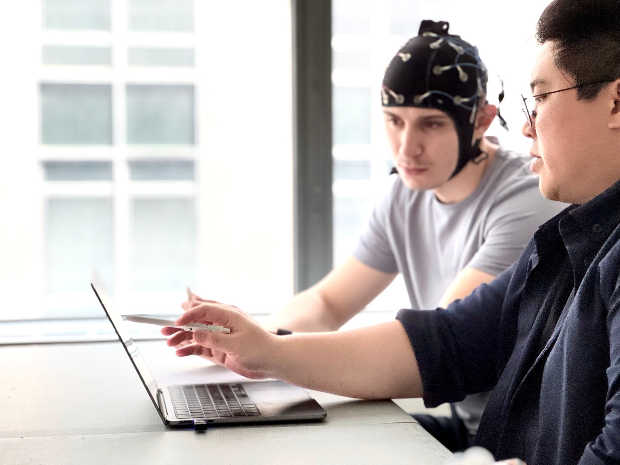 An EEG practitioner reviewing brain mapping results with a participant wearing an EEG cap